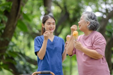 Yaşlı kadın ve genç hemşire, açık hava parkında dondurmanın tadını çıkarıyorlar.