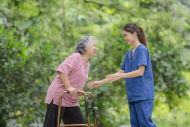 Yürüteçli yaşlı kadın, açık hava parkındaki genç hemşireden bakım desteği alıyor..