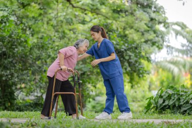 Elderly woman with walker receives caring support from young nurse in outdoor park setting clipart