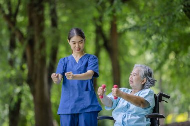 Nurse Guiding Elderly Woman in Wheelchair Through Dumbbell Exercises, Enhancing Strength and Mobility Outdoors clipart