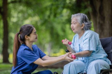 Nurse Guiding Elderly Woman in Wheelchair Through Dumbbell Exercises, Enhancing Strength and Mobility Outdoors clipart