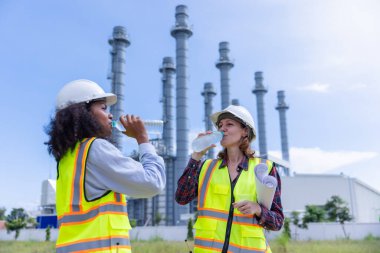 Two Female Engineers Hydrating During a Break at an Industrial Power Plant Construction Site clipart