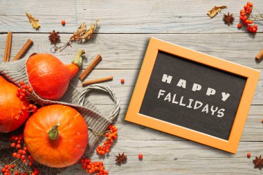 Tahtada Mutlu Yıllar mesajı, tebeşir tahtası. Turuncu Hokkaido kabağı, rowan üzümü, elma, tarçın. Eski ahşap üzerinde sonbahar dekoru. Düzlük, üst manzara, Sonbahar mevsimi arka planı sıcak doğal renklerle.