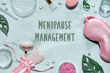 Menopoz yönetimi metni, sağlığın düzleşmesi üzerine. Pembe taş yüz silindiri ve nane yeşili üzerinde canavar yapraklı Guasha taşı. Havlu, uyku maskesi, cam petri kabında nemlendirici..