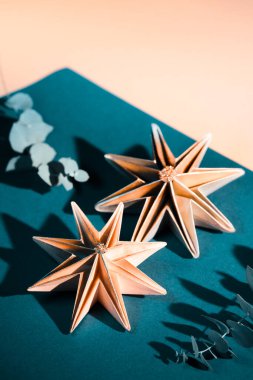 El yapımı kağıt yıldızlar, kendi kendine yapılmış Noel süslemeleri. Koyu yeşil, turkuaz ve kokulu okaliptüslü altın sarısı arka planda Xmas süsleri. Origami zanaat hobisi.