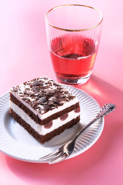 Chocolate cake and glass of pink, rose wine on pink background. Choco torte with white cream and sour cherries. Piece of cake on a plate with fork. Sweet dessert on vibrant pink background.