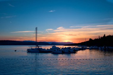 Hırvatistan 'ın Dalmaçya kentindeki Adriyatik kıyısında gün batımı. Tekneli iskele silueti. Arka planda Krk adasında günbatımı. Rijeka 'nın Jadranovo köyü, Primorje Gorski Kotar bölgesi.