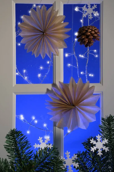 简单的纸制圣诞星和挂在窗户上的灯 装饰过的圣诞窗户外面有蓝色的黄昏灯 有雪花的冷杉枝条 手工制作的纸 瑞典式的星星和花环 手工制作的斯堪的纳维亚装饰 — 图库照片