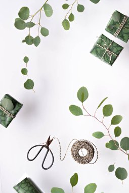 Eucalyptus twigs and gift boxes with wrapping paper isolated on white background. Flat lay, top view overhead. Scissors with reel of stripy gold white cord.