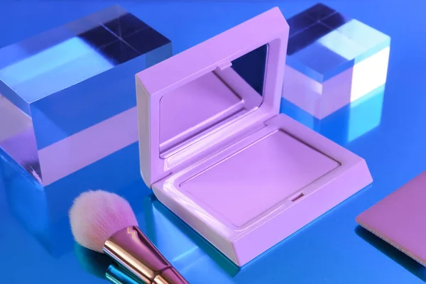 Mockup of a beauty product featuring a blush box with a mirror and cosmetic brush, set against a blue geometric background with acrylic cubes