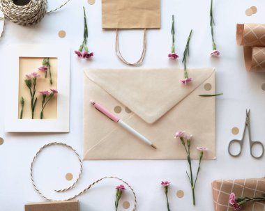 Zarf ve kendi kendine hazırlanmış tebrik kartı konsepti. Karanfil çiçeği desenli. Knoling tarzı. Paketlenmiş hediye, kağıt kartpostal, kağıt zarf, kablo, makas ve mor karanfiller..