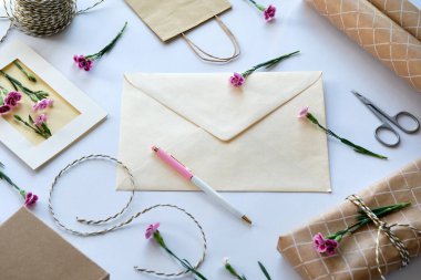 Zarf ve kendi kendine yapılmış tebrik kartı konsepti, taze karanfil çiçekleriyle. Paketlenmiş hediye, kağıt kartpostal, kağıt zarf, kablo, makas ve mor karanfiller..