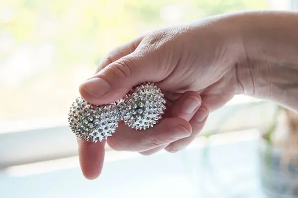 Silver metal magnetic balls in female hand. Spiky tool for hand massage. Close-up on middle-aged hand.
