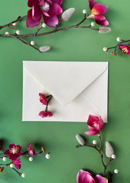 鮮やかな緑の背景に配置された繊細なピンクのマグノリアと梅の花で飾られた白い封筒 — ストック写真