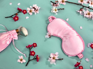 Uyku kalitesi ve kişisel bakım rutini. Uyku maskesi, masaj taşı silindiri ipek çantada bahar çiçekleri renkli kağıt arka planda