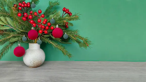 冬季布置 在绿墙旁边的木制桌子上放上冷杉枝条 圣诞装饰品和红色的野越橘 全景图像 复制空间 — 图库照片