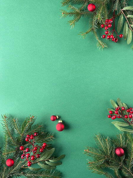 A festive green background adorned with vibrant red berries, greenery, fir twigs, and rowanberries. Baubles and Christmas decorations create a visually appealing composition with ample copy space.