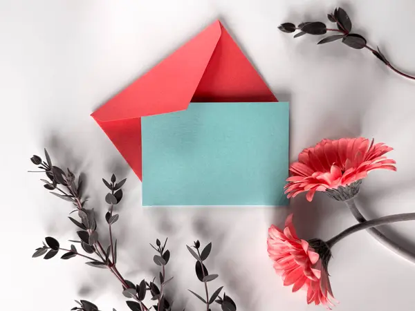 赤い花と白い表面に配置された青い封筒は 対照的で活発な構成を作成します グリーティングカードのコピースペース — ストック写真