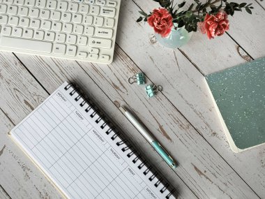 Boş bir haftalık ajandası, bilgisayar klavyesi ve üstünde çalışmaya hazır bir not defteri olan bir masa..