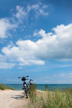 Bir bisiklet tozlu toprak bir yolun kenarında duruyor, çiçek açmış bahar çiçekleriyle çevrili. Baltık Denizi 'nin romantik kıyıları.