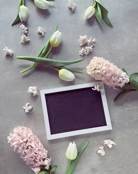 A blank blackboard picture frame surrounded by fragrant spring flowers, white tulips and pink hyacinth.