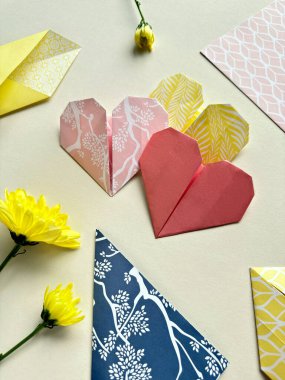Colorful Origami Hearts in Varying Patterns Arranged Near Envelopes on Pastel Background. clipart