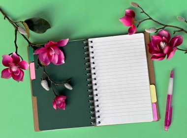 Yeşil Arkaplanda Pembe Çiçekler ve Kalemle Not Defteri Aç.