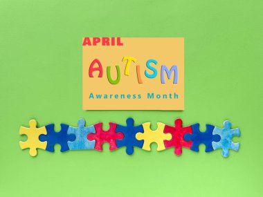 Otizm Farkındalığı Ay tasarımı. Yeşil arkaplanda iç içe geçmiş renkli yapboz parçaları var. Canlı renklerde 