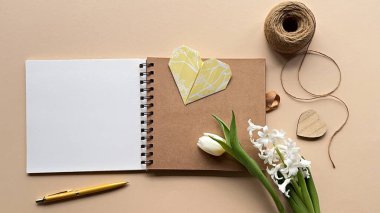 Kapağında sarı bir kalp olan spiral bir defter aç. Beyaz sümbül çiçekleri, bir lale, bir kalem ve bej bir yüzeye dizilmiş bir sicim..