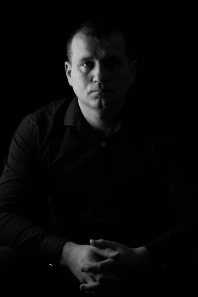 Black and white photo of a man in a shirt on a black background.