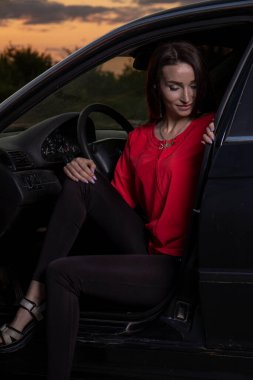Gün batımının arka planında arabanın yanında güzel genç bir kız..