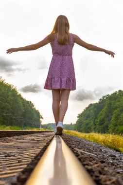 Elbiseli bir kız raylar boyunca yürüyor..