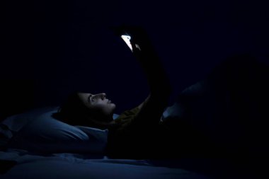 Yatakta beyaz yatağı ve telefonu olan güzel bir genç kız..