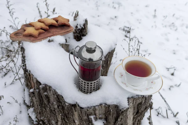 Tea in a teapot on a snowy forest meadow with a house.