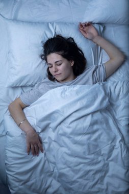 Güzel bir kız beyaz çarşaflı bir yatakta uyuyor..