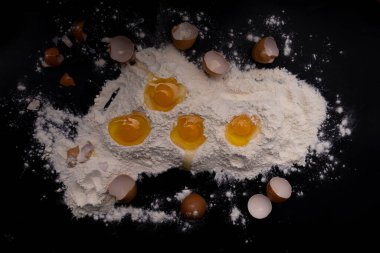 Siyah arka planda un ve kırılmış tavuk yumurtaları..
