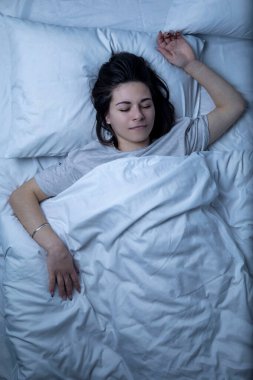 Güzel bir kız beyaz çarşaflı bir yatakta uyuyor..