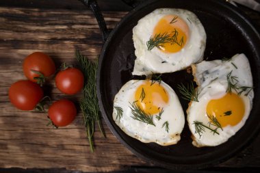 Tavada pişmiş yumurta, siyah arka planda sebze ve otlar.