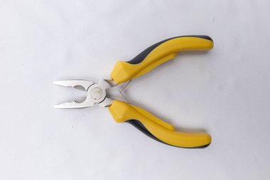 Basit beyaz arka plan üzerinde dinlenen küçük sarı saplı pense, çeşitli el işi ve onarım projeleri için ideal.