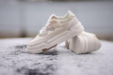 Bej aksanlı modern spor ayakkabıları kar tozlu bir yüzeyde sergileniyor, tasarımlarını sergiliyorlar.