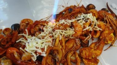 Kajun bbq soslu deniz ürünleri kovası. Peynir sosu. Bol miktarda eritmek için yanan meşale kullanılıyor.