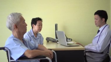Asyalı yaşlı çift hastanede doktorla görüşüyor. İlaç seçimi için endişeleniyorlar.