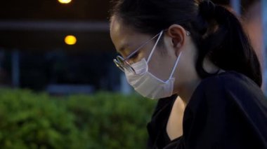 Asyalı kadın gece maske takıp beklerken akıllı telefon kullanıyor.