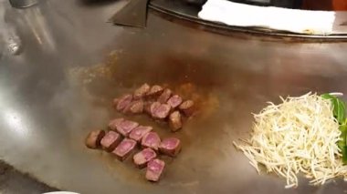 Teppanyaki metal tabak üzerinde Kobe bifteği et ve fasulye filizleri pişiren şef.