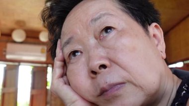 Asyalı yaşlı bir kadın endişeli. Yüzünde kapanık bir ifade var. Hayatı düşünüyor.