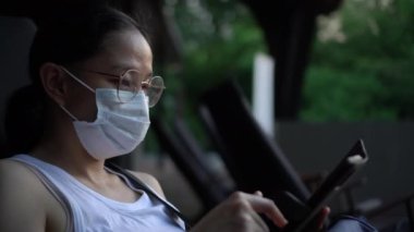 Asyalı kadın akıllı telefon kullanarak gözlük takıyor ve maske takıyor. Sosyal medyaya bakıyor ve partneriyle konuşuyor.
