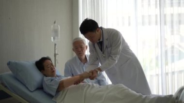Asyalı doktor yaralanan yaşlı kadını kontrol et. Kadın hastane yatağında. Kocası fiziksel olarak endişeleniyor.