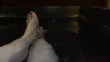 Kadın ayakları hareket ediyor. Rahatlayın. Küvette sıcak su tedavisinin tadını çıkarın.