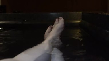 Kadın ayakları hareket ediyor. Rahatlayın. Küvette sıcak su tedavisinin tadını çıkarın.