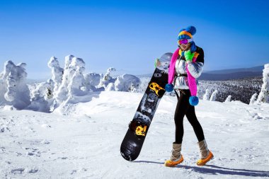 Kız snowboardcu kayak merkezinin tadını çıkarıyor. Kış kıyafetli güzel bir kadın dağlarda snowboard ile poz veriyor. Kış sporları. Snowboard..